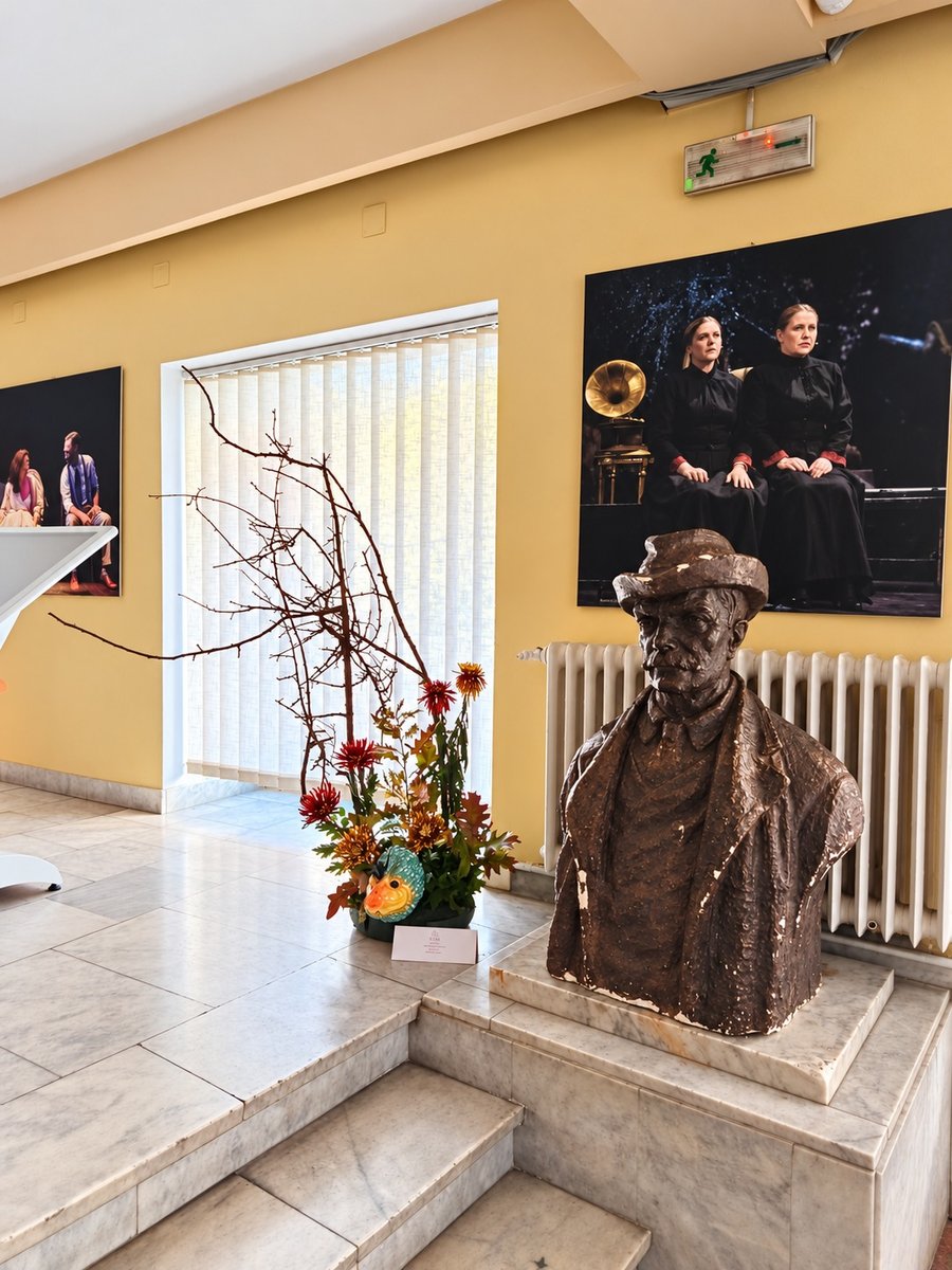 Aranjament cu ramuri și crizanteme de toamnă lângă un bust din foaierul teatrului