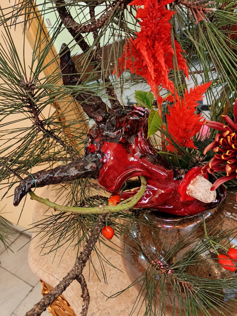 Sculptură ceramică roșie între ramuri de pin și celosia
